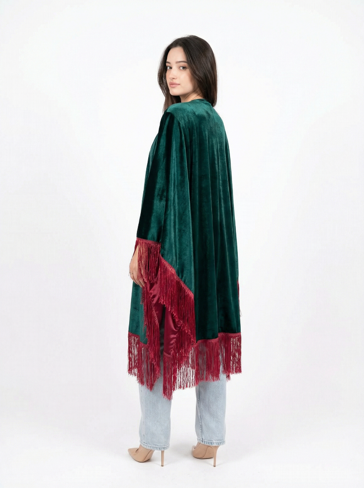 Woman wearing a green velvet poncho with red fringe on a white background