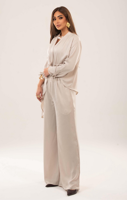 A woman wearing a beige wrap top with long sleeves and matching wide-leg trousers, standing against a neutral background.
