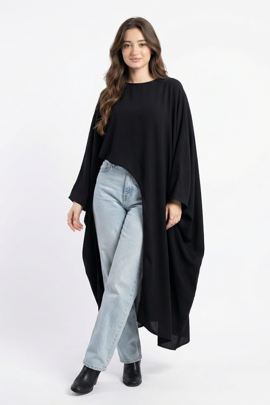 Woman wearing a black poncho over a black top and light blue jeans on a white background