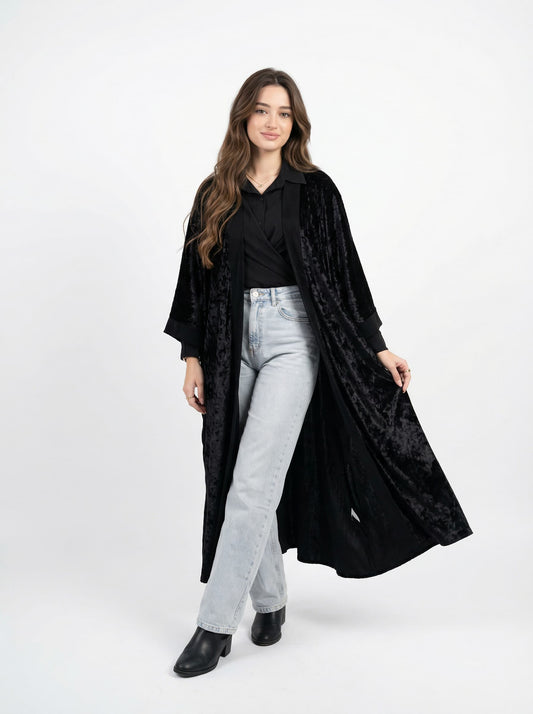 Woman wearing a black long coat over a black shirt and light gray jeans on a white background