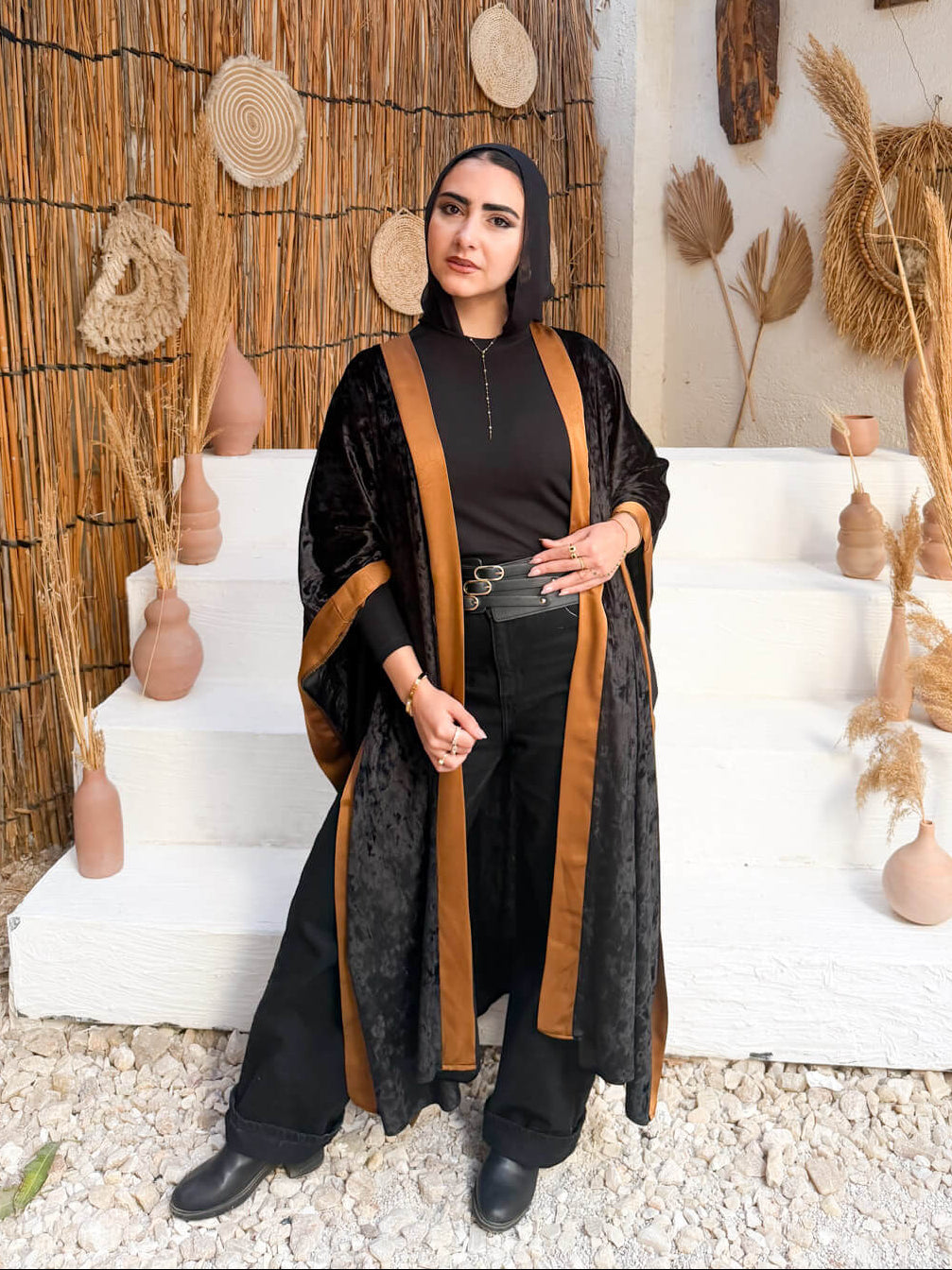 Woman in a black and brown outfit standing in a rustic setting with decorative elements.