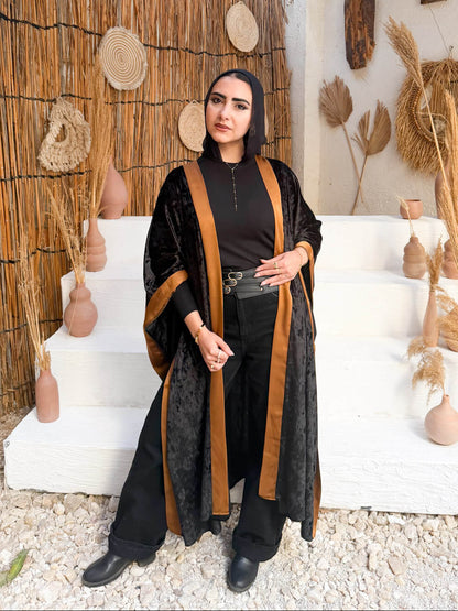 Woman in a black and brown outfit standing in a rustic setting with decorative elements.