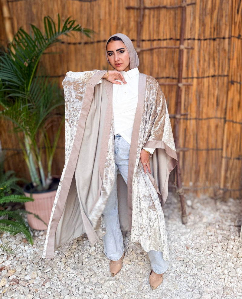 Woman wearing a beige embroidered cover-up in an outdoor setting with plants and a wooden wall.