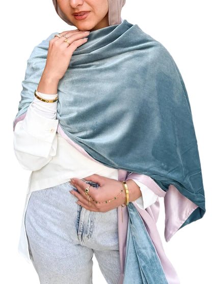 Woman wearing a light blue shawl over her shoulders with a wooden wall and plant in the background