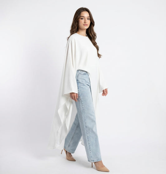 Woman wearing a white cape over a light blue denim outfit on a plain background