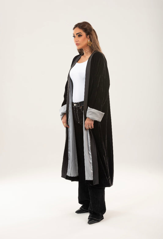 Woman wearing a long black and gray cardigan over a white top and black pants on a white background